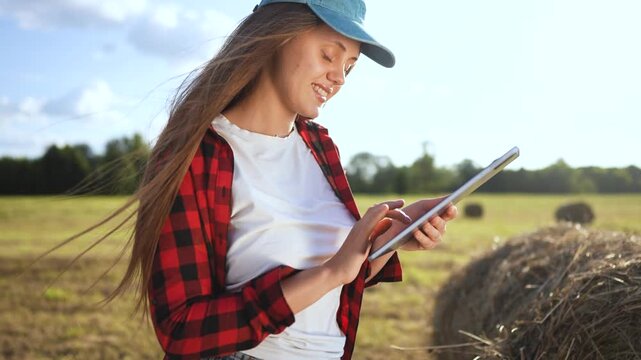 Woman in field holding tablet computer. Girl works on tablet in field. Woman works in a field with haystacks of grass. A lifestyle woman in a field is holding a tablet.
