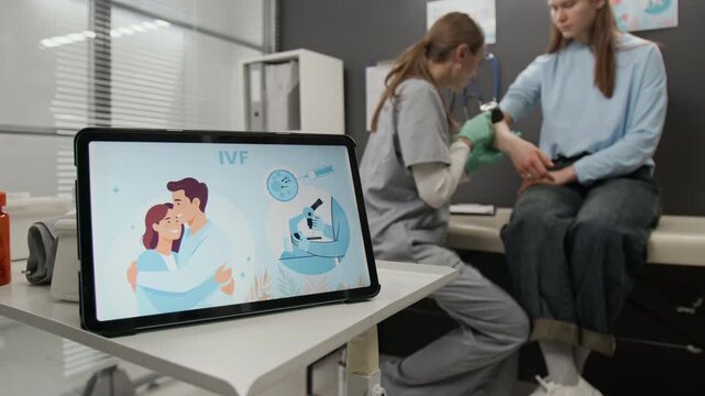 Close-up shot of digital tablet displaying educational IVF illustration in foreground, healthcare professional in scrubs examining patients skin in background