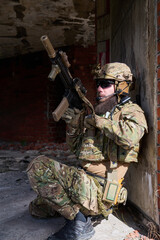 Obraz premium Armed Tactical Soldier In Camouflage Gear With Rifle Taking Cover In Urban Ruins