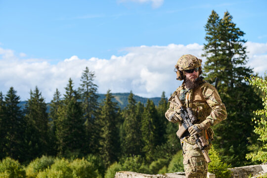 Armed Special Forces Soldier in Multicam Camouflage Standing in Forest Mountain Landscape