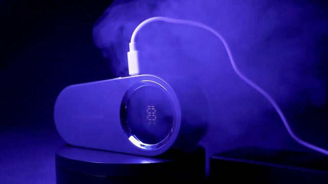 A portable humidifier charges via USB cable while releasing a steady stream of mist against a dark background. Concept of modern technology, air purification, and smart home electronic gadgets