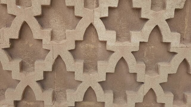 Close-up view of an ornate mosque wall in Morocco featuring intricate geometric Islamic patterns carved in warm-toned stone. 