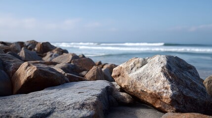 Naklejka premium Massive weathered boulders stretch along the rocky coastline meeting the calm blue ocean waves under a clear sky