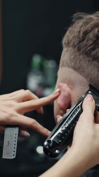 Close-up of barber using electric clippers to trim mans hair, precise grooming process in barbershop focusing on clean fade haircut and professional styling
