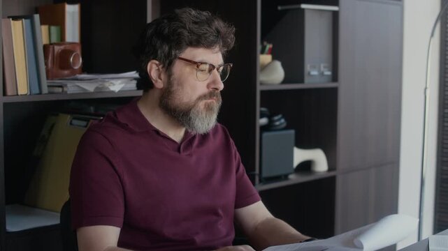 Medium shot of middle aged Caucasian male author looking through papers and thinking over plot plan