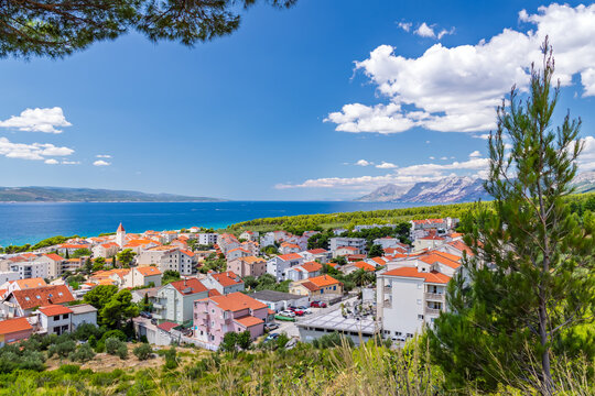 Panoramic view of Baska Voda town on the Adriatic coast in Dalmatia, Croatia, featuring red-roofed houses, blue sea, and mountains under a clear summer sky