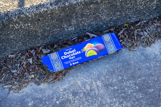 Title:
Iserlohn, Germany &mdash; April 29 2026: a blue cardboard packaging of Boujee Dubai Chocolate Style dessert lying on a pavement with dry leaves.