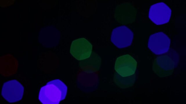 Blue, green and violet bokeh lights on black start bright, fade , return brighter midway, dim again, then finish vivid with slight drifting motion.