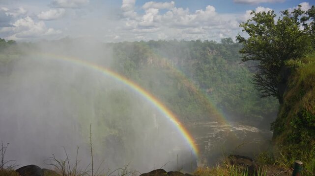 Double rainbow arching over magnificent Victoria Falls on Zambezi River, powerful water spray and lush green landscape between Zimbabwe and Zambia in Africa