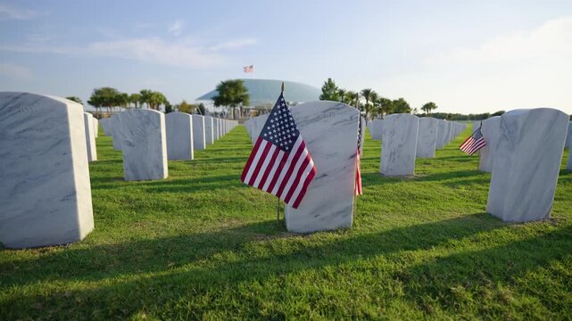Military burial headstones. Sarasota National Cemetery with rows of white tomb stones and USA flags on green grass. Memorial Day concept.