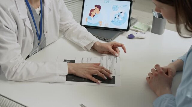 Gen Z girl discussing ultrasound results with female fertility doctor at white desk while visiting reproductive center