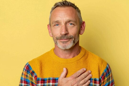 Mature man demonstrating breathing exercise with hand on chest against yellow background