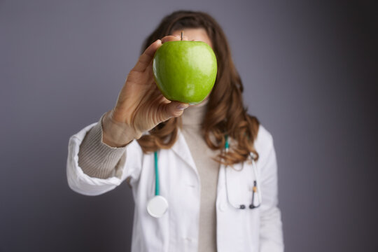 A female doctor holds a green apple to emphasize the link between diet and health. A creative shot perfect for nutritionists, dietitians, and wellness campaigns.