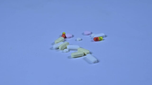 A hand reaches into a pile of diverse medicinal pills and selects a pink tablet.