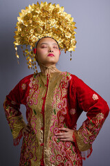 Fototapeta premium Portrait Of Indonesian Asian Woman Wearing Ornate Gold Headdress And Red Traditional Costume Celebrating Cultural Ceremony