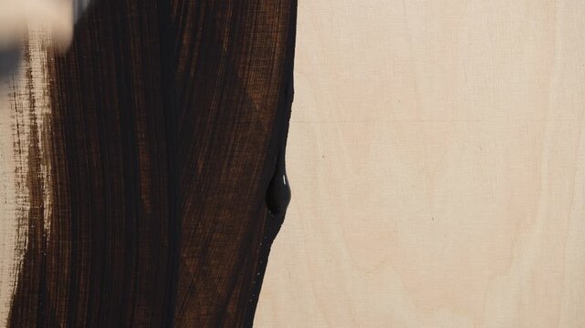 Close up of applying dark stain to a light wooden surface with a brush. Concept of woodworking home renovation and DIY furniture restoration