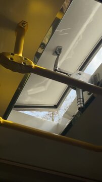 Public transport ceiling vent mechanism closing steadily, showing mechanical operation of an upper panel, restricting bright daylight, adjusting interior environment.