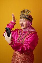 Fototapeta premium Excited Young Indonesian Asian Woman in Hijab and Traditional Costume Taking a Selfie on Yellow Background