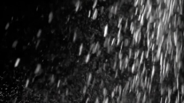 Pristine, luminous white particles, from microscopic dust to flakes, gently drift diagonally against a deep black void background with shallow depth of field. Ethereal light phenomena concept