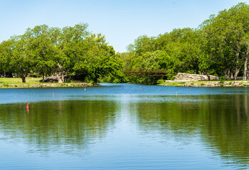 Obraz premium A tranquil view of a clear lake reflecting the surrounding greenery and a small bridge. Serene waterscape in Legacy Hills Park, Georgetown, Texas.