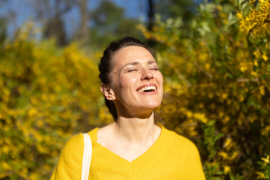 A radiant woman with eyes closed enjoys the warmth of a sunny spring day, surrounded by yellow blossoms. This portrait captures the essence of freedom and outdoor bliss.