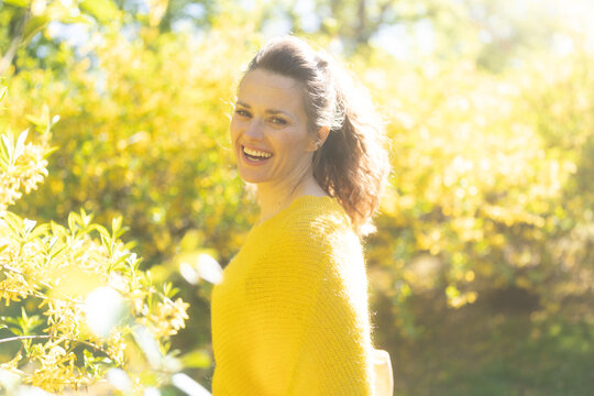 A radiant woman smiles broadly in a sunny, blooming garden, embodying pure happiness, mental wellness, and the refreshing spirit of springtime.