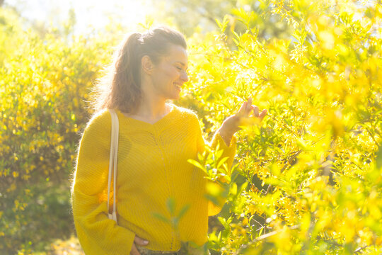A woman gently touches yellow forsythia blossoms, feeling the fresh energy and harmony of spring nature in this joyful, sun-kissed garden scene.