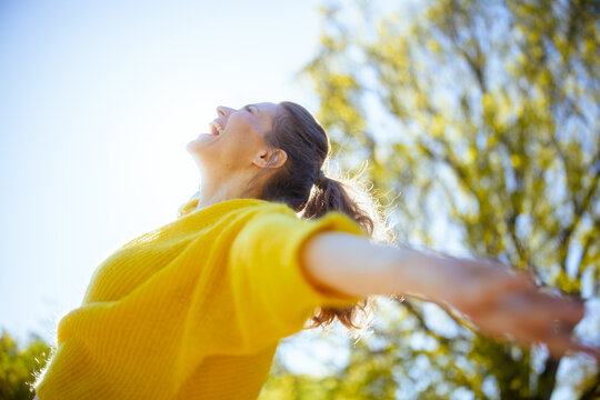 A woman laughing and stretching arms wide in a sunlit spring park, capturing the essence of freedom, joy, and emotional wellbeing.