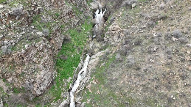 4K aerial drone footage of cascading waterfall in rocky mountain canyon, flowing stream through natural landscape.