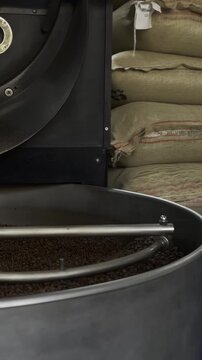 Processo de torrefa&ccedil;&atilde;o industrial de caf&eacute;. Gr&atilde;os de caf&eacute; torrados girando no resfriador da m&aacute;quina com sacas de caf&eacute; cru ao fundo em uma cafeteria ou torrefa&ccedil;&atilde;o.