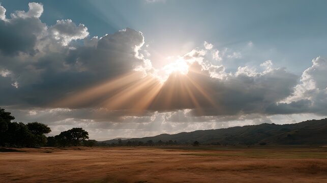 A dramatic sky captures golden sun rays breaking through heavy clouds over an expansive open field landscape