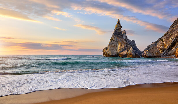 Portugal Ursa Beach at atlantic coast of Atlantic Ocean with rocks and sunset sun waves and foam at sand of coastline picturesque landscape panorama..