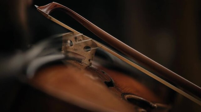 A close up shot of a hand holding a violin bow poised to touch the strings of a wooden violin from file w3 Ha34X 231 chr2 prob4.