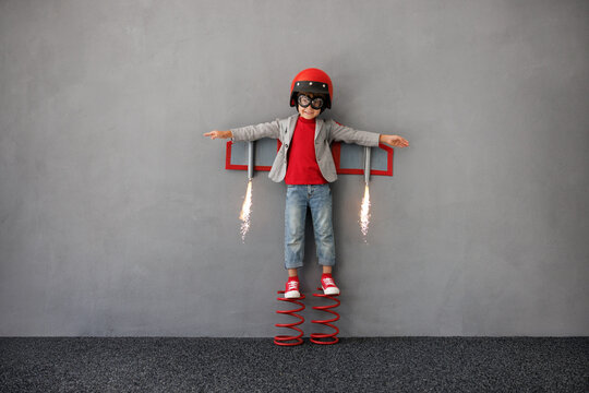 Happy child playing with paper rocket against grey wall background. Kid having fun indoors. Funny boy pretend to be astronaut. Imagination and children dream concept