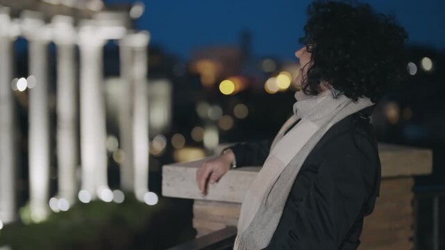 Stylish happy woman smiling at camera on night tour of Roman forum with background view of Tample of Saturn in Rome, Italy, slow motion
