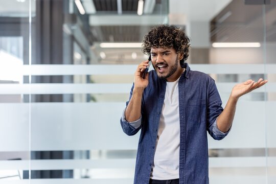 Indian young man standing in office, talking on phone aggressively and emotionally