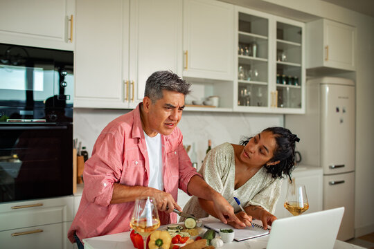 Couple cooking with laptop in modern home kitchen