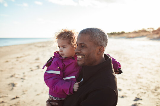 Smiling father holding daughter on sunny beach