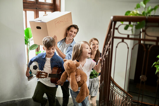 Happy parents and children carrying boxes up apartment stairs