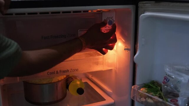 close up of a hand adjusting the temperature control knob inside a domestic refrigerator