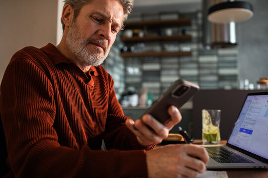 Senior man managing finances on smartphone at home office