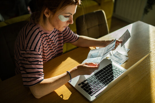 Young woman reviewing household bills at home with laptop