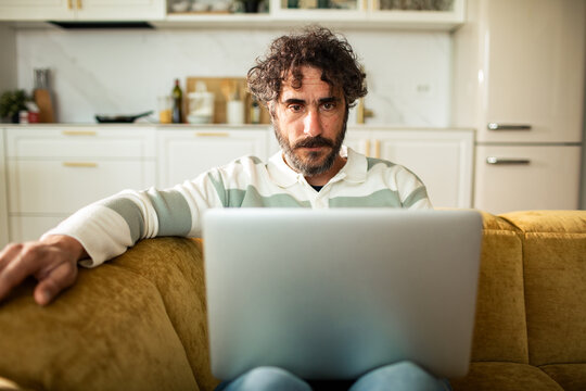 Focused man working on laptop on sofa in home kitchen