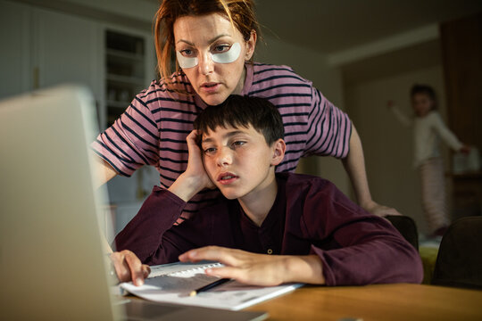 Tired mother helps bored son with homework at kitchen table