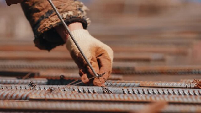 Worker tying steel rebar with wire on reinforcement grid close up