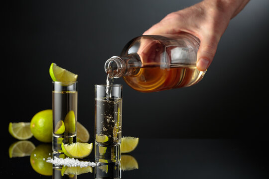 Tequila shots with salt and lime slices on a black reflective background.