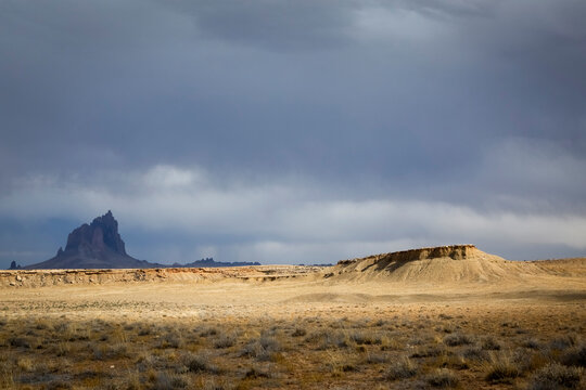 Wide desert landscape with distant Shiprock formation and dramatic storm clouds