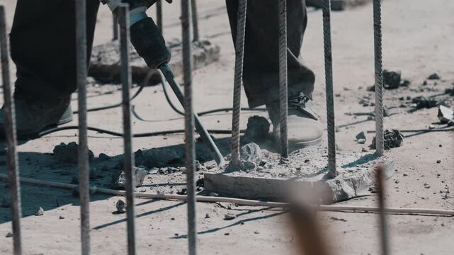 Breaking concrete around rebar with electric jackhammer during construction close up