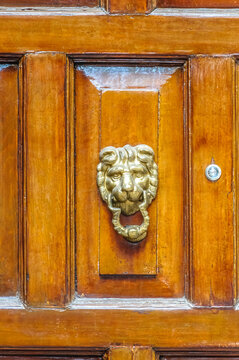 Lujosa aldaba de lat&oacute;n dorado con cabeza de le&oacute;n en puerta de madera antigua pulida. Concepto de seguridad, tradici&oacute;n y elegancia hist&oacute;rica.
