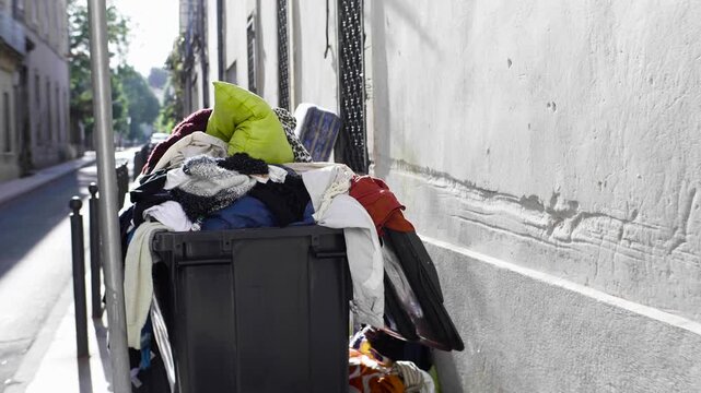 poubelle pleine d&eacute;borde a ras bord dans rue avec soleil , Poubelle ext&eacute;rieure d&eacute;bordante remplie de v&ecirc;tements en plein soleil
